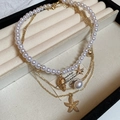 Dettaglio dei ciondoli a stella marina e conchiglia con collana di perle in scatola regalo - Set da 3 pezzi in oro (HN8370)