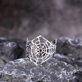 Macro view of silver spider web cuff bracelet on a dark textured rock surface - Silver