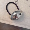 Nahaufnahme eines hochglänzenden Goldmetall-Accessoires auf einem lila Haargummi - Glattes Oval / Silbernes Oval