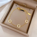 Detail van een goudkleurige titaniumstalen armband met witte zirkoon in een beige doosje - Goud