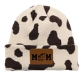 Close-up of knit beanie featuring cow print pattern and brown leather MOM patch - Dalmatian Beige/Dark Brown Cow