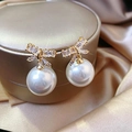 Dettaglio macro di orecchini a fiocco dorati con cristalli e grande perla bianca - Bianco (Stile Fiocco)