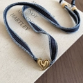 Detail of a golden heart pendant on a blue denim strap with visible white stitching - Denim Blue Style (Necklace - Blue)