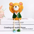 Detail of yellow resin bear figurine in green suit sitting on decorative books - Hear-no Bear
