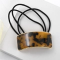 Detailed close-up of tortoise shell square buckle hair tie with gold trim on white surface - Amber