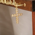 Primo piano del ciondolo a croce dorata con zirconi lucidi su supporto in legno - Stile Croce 25