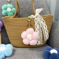 Detail of colorful plush flower charms with gold hardware on a woven straw bag - Pink