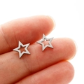 Macro shot of silver cutout star stud earrings held on fingertips to show small size - Steel