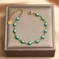 Macro detail of gold stainless steel heart charm with S.Steel engraving and green evil eye bead - Green