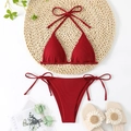 Detailed flat lay of a burgundy ribbed halter bikini set on a woven mat with summer decor - Red