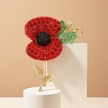 Detailed view of a red and black poppy flower brooch with green crystals on a gold stem - Poppy