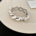 Detailansicht der dicken versilberten Armspange mit poliertem Drehdesign auf weißem Porzellan - Spiralverdrehung / Silber
