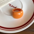 Dettaglio di un anello geometrico in resina arancione su un piatto di ceramica decorato - Arancione