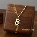 Titanium steel necklace featuring a gold letter B pendant and tassel on wooden stand - Letter B / Gold