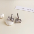 Close-up of silver bow hoop earrings with heart-cut zircons on decorative white stones - Rhodium Plated Silver Bow Knot Zirconia Studs