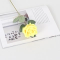 Vibrant yellow artificial velvet rose with green leaves on an open magazine - Silk Yellow