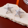 Close-up of star-shaped crystal earrings with silver setting on a natural beige stone - Silver