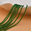 Close-up of 2mm faceted green crystal beads hanging from a white ceramic plate - Grass Green