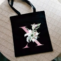 Black canvas tote bag featuring a pink letter X with white lily floral print design - Letter X / Black