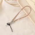 Detail of champagne gold rhinestone phone lanyard with silver metal clasp on beige fabric - Champagne