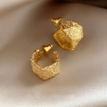 Detail of gold geometric C-shaped earrings with textured surface on beige silk fabric - Gold