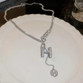 Macro detail van de zilveren H-letter ketting met kristallen op keramisch bord - Ketting met strass H-letter en asymmetrische ketting / Zilver