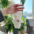 Close-up of white plush bear keychain with pink heart detail held in hand - White Bear With Golden Buckle & Pink Heart