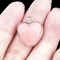 Pink heart-shaped gemstone pendant with silver metal bezel held by fingers - Rose Quartz Silver Edging