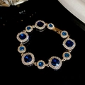 Makroaufnahme von vergoldetem Armband mit blauen Kristallen und funkelndem Zirkonia-Rand - Armband-Gold-Blau