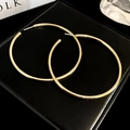 Close-up of minimalist large gold hoop earrings on black leather texture background - Silver Earring Post Regular Gold Quilted Hoop