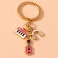 Detailansicht goldener Schlüsselanhänger mit rosa Gitarre, Klavier und Kopfhörer - Rosa