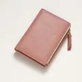Close-up of pink bi-fold wallet featuring gold embossed text and side metal zipper pocket - Pink