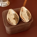 Detailed view of golden leaf-shaped earrings on a brown velvet surface with glossy finish - Gold / Gold