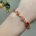 Close-up of golden bracelet featuring red enamel hearts and clear zircon stones on wrist - Red