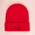 Detailed close-up of red knit beanie featuring black embroidered smiley face patch - One Size / Red