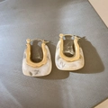 Detail of golden U-shaped earrings with white marble resin inlay on dark background - Cream