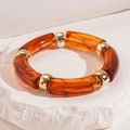 Macro detail of amber acrylic tube beads and gold metal spacers on a stone surface - Bracelet - Dark Coffee