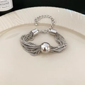Makroansicht der silbernen mehrsträngigen Box-Kette mit Kugelperle auf Keramikteller - Armband - Silber