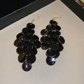 Detalle macro de pendientes de discos negros con ganchos dorados sobre fondo gris - Negro