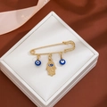 Detail of golden Hamsa Hand and blue Evil Eye charms on a pin brooch in a white gift box - Classic Hamsa Style (Z81)
