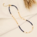 Dettaglio della collana in pietre naturali e perle su tessuto bianco con decoro di grano - Blu Reale