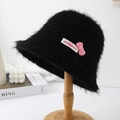 Detail of black faux fur bucket hat with pink bow and woven label on a wooden stand - Black