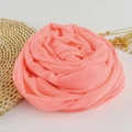 Coral pink linen cotton scarf folded into a rose shape on a rustic woven mat with yellow flowers - 190x100cm / Watermelon Red
