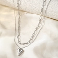 Detail view of silver double-layered paperclip chain with heart pendant on soft fabric - Cross O-Chain Heart / Steel