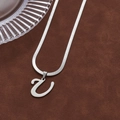 Silver snake chain necklace with an abstract letter pendant on brown leather texture - Letter U