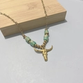 Bohemian gold bull skull necklace featuring green beads on a rustic wooden background - Bull Head