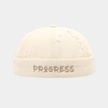 Macro shot of PROGRESS embroidery and distressed details on cream brimless cap - Adjustable / Beige