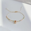 Detail eines verstellbaren Regenbogen-Perlenarmbands mit goldenem 3D-Buchstaben E - Buchstabe E