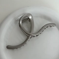 Close-up of a silver matte metal claw clip in a streamlined shape on a white plate - Grey Silver - Y-Shape