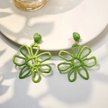 Detailed view of handmade green woven raffia flower earrings on a white display tray - Green